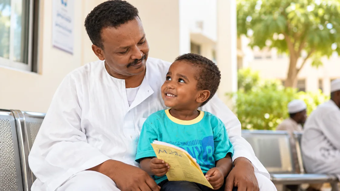 A father and his young son sitting together outside an Al Basar hospital